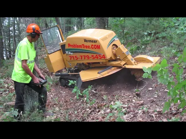 Operator in a hard hat using a remote to run a Vermeer stump grinder on a wooded slope